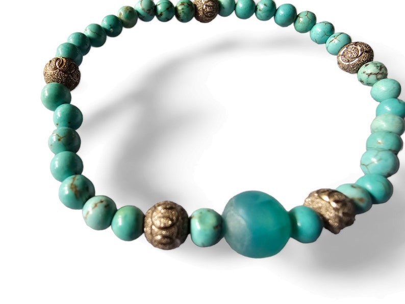 May include: Turquoise blue beaded bracelet with silver accents. The bracelet features a large turquoise blue bead in the center.