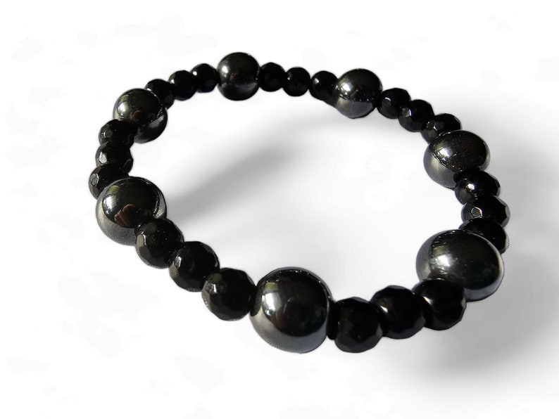 Op de afbeelding: Een zwarte kralen armband met afwisselende grote en kleine kralen. De grote kralen zijn rond en hebben een glanzende, metallic afwerking. De kleine kralen zijn gefacetteerd en hebben een matte afwerking.