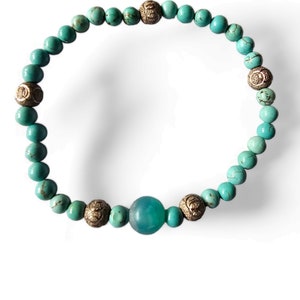 May include: A turquoise and gold beaded bracelet with a larger turquoise bead in the center.