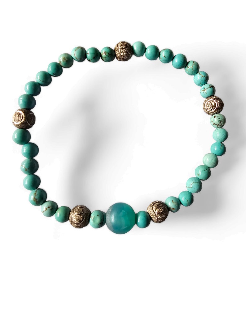 May include: A turquoise and gold beaded bracelet with a larger turquoise bead in the center.