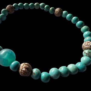 May include: A turquoise beaded bracelet with silver accents. The bracelet has a large turquoise bead in the center.