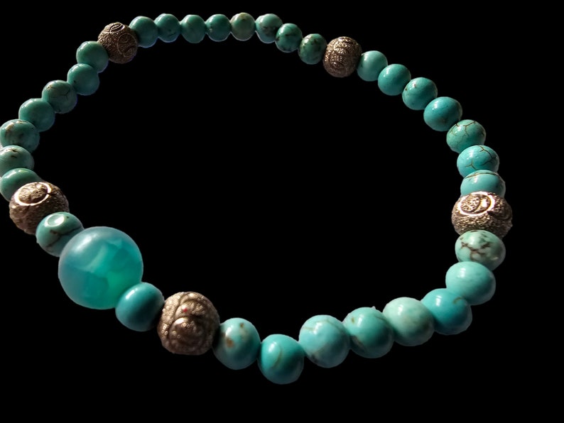 May include: A turquoise beaded bracelet with silver accents. The bracelet has a large turquoise bead in the center.