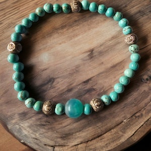 May include: A turquoise and gold beaded bracelet with a large turquoise stone in the center.
