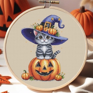 May include: A gray and white kitten wearing a blue witch hat with stars sits on top of an orange jack-o'-lantern pumpkin. The pumpkin has a carved face with a wide smile. There are smaller pumpkins around the base of the large pumpkin.