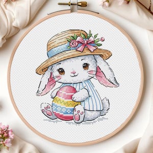 May include: A white bunny wearing a straw hat with a blue ribbon and pink flowers, holding a colorful Easter egg.