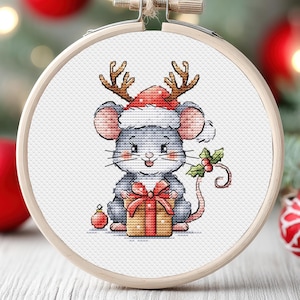 Könnte beinhalten: Eine graue Maus mit einem roten und weißen Weihnachtsmann-Hut mit Rentiergeweih hält ein verpacktes Geschenk mit einer roten Schleife. Die Maus hält das Geschenk in ihren Vorderpfoten und hat einen glücklichen Gesichtsausdruck.