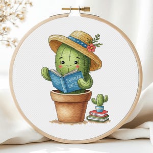 Puede incluir: Un lindo cactus de dibujos animados con un sombrero de paja con lunares azules y leyendo un libro titulado "Summer Cacti". El cactus está en una maceta marrón y tiene un pequeño cactus con una maceta roja a su lado.