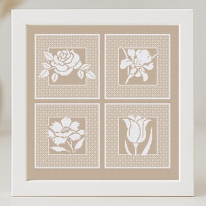 May include: A white framed picture with four beige squares, each containing a white embroidered flower design. The flowers are a rose, a tulip, an iris, and a daisy.