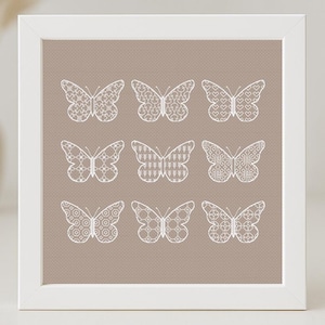 Puede incluir: Una imagen enmarcada en blanco con un fondo beige que presenta nueve mariposas blancas con intrincados patrones. Cada mariposa tiene un diseño diferente.