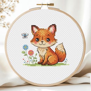 May include: A cross-stitch embroidery hoop featuring a cartoon fox with orange and white fur, sitting in a grassy area with flowers and a butterfly. The embroidery is set in a round wooden hoop.