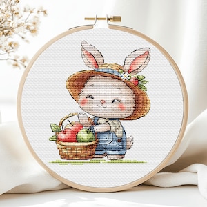 May include: A cute cartoon bunny wearing a straw hat and overalls is holding a basket of apples. The bunny has a pink nose and cheeks and is smiling.