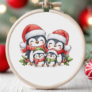 Puede incluir: Un patrón de punto de cruz con una familia de pingüinos que llevan gorros de Papá Noel y bufandas. Los pingüinos están de pie sobre un fondo nevado con hojas de acebo y bayas.
