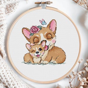 May include: Cross stitch pattern of two brown and white corgis cuddling. The larger corgi has a pink flower crown and a butterfly behind it.