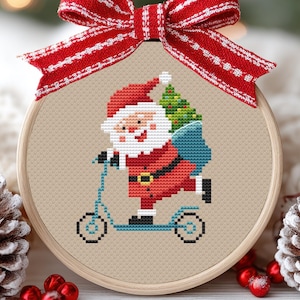 May include: A cross-stitch embroidery hoop depicting Santa Claus on a blue scooter, with a Christmas tree and gifts. The design is on beige fabric, framed by a wooden hoop, and decorated with a red and white striped bow. A festive Christmas decoration.