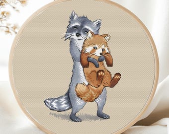 Op de afbeelding: Een kruissteek borduurpatroon met een wasbeer die een rode panda vasthoudt. De wasbeer is grijs met zwarte markeringen en de rode panda is oranje en wit.
