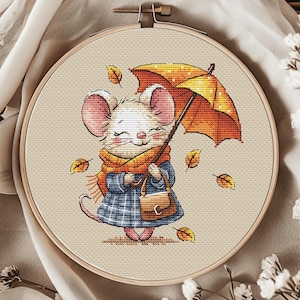 以下が含まれることがあります： 青いチェック柄のコートとオレンジ色のマフラーをつけたかわいい漫画のネズミが、白のドット模様のオレンジと黄色の傘を持っています。ネズミは落ち葉のフィールドを歩いています。