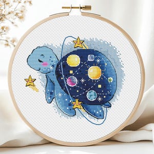 May include: A blue turtle with a galaxy design on its shell. The turtle is surrounded by stars and planets. The design is stitched on a white canvas.
