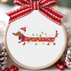 May include: A cross-stitch pattern of a dachshund wearing a Santa hat and tangled in Christmas lights. The pattern is framed in a round wooden hoop.