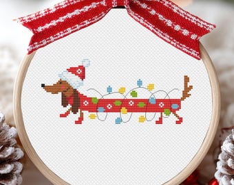 May include: A cross-stitch pattern of a dachshund wearing a Santa hat and tangled in Christmas lights. The pattern is framed in a round wooden hoop.