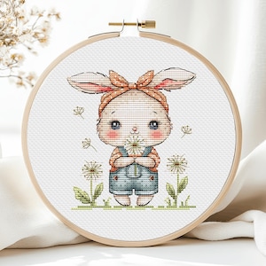 May include: A cross-stitch embroidery hoop with a cute cartoon bunny wearing a blue overall and an orange headband. The bunny is holding a dandelion and surrounded by dandelions.
