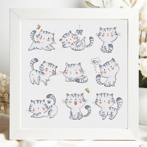 May include: A framed artwork featuring nine adorable cartoon cats in various poses. The cats are primarily white with gray stripes and pink accents. Some cats interact with butterflies or think bubbles. The artwork is set in a white frame.