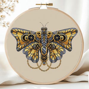 May include: A gold and gray steampunk butterfly cross stitch pattern on a beige background. The butterfly is made of gears and chains.