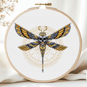 May include: A gold and silver embroidered cross-stitch pattern of a moth with a skull head, surrounded by a circular mandala design.
