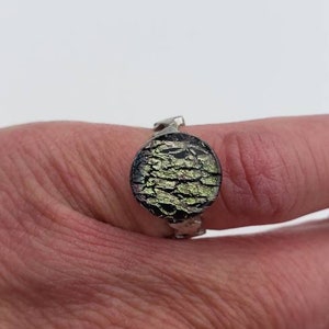 May include: A silver ring with a round, green and black glass stone. The stone has a textured, cracked surface.