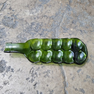 May include: A green glass bottle repurposed into a serving dish with eight indented sections. The bottle has a rounded, wavy shape.