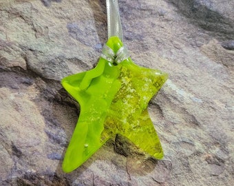 May include: A lime green glass star ornament with a silver ribbon attached. The star has a sparkly, glittery texture.