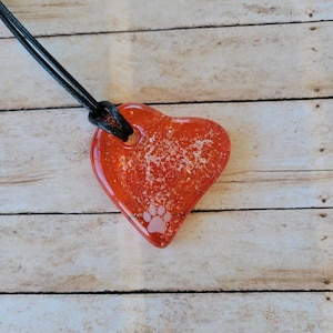 May include: A heart-shaped pendant necklace with a red, translucent resin heart. The heart has a paw print and glitter embedded within. The necklace has a black cord.