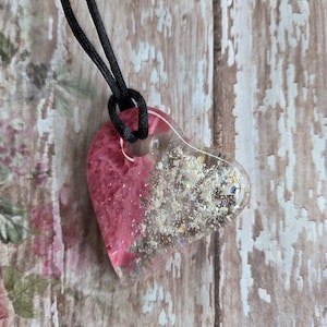 May include: A heart-shaped pendant necklace with a black cord. The pendant is clear resin with pink and silver glitter accents. The pink resin fills the left side of the heart, while the right side is clear with glitter.