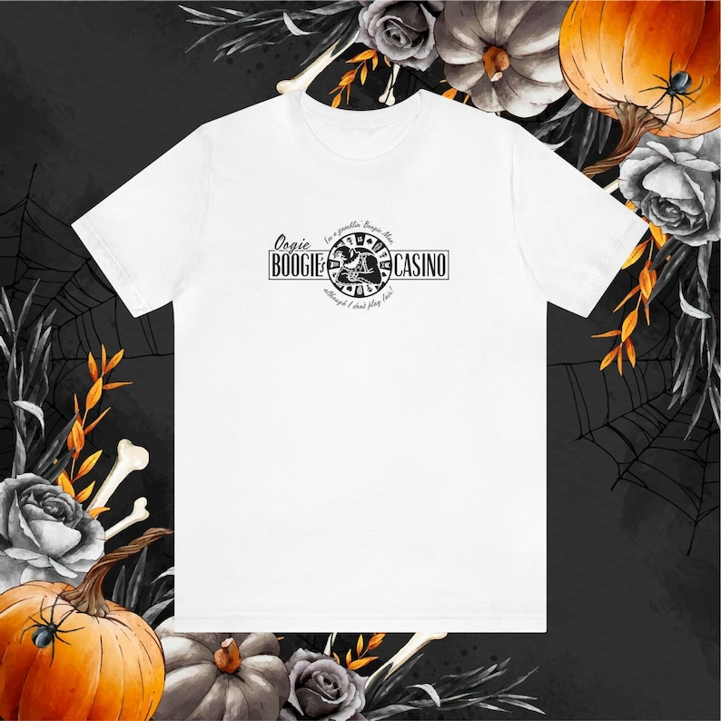 Pu&ograve; includere: T-shirt bianca con grafica nera che recita "Oogie Boogie Casino" con un design circolare e il testo "I'm a gambler, Boogie Man, although I don't play fair!". Abbigliamento a tema Halloween.
