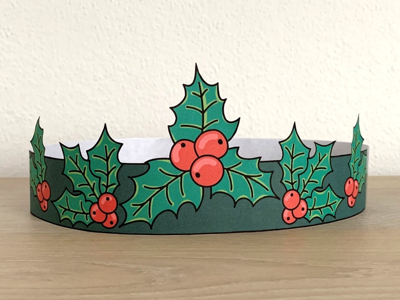 May include: A green paper crown with red holly berries and green leaves. The crown is designed to be worn as a festive accessory.
