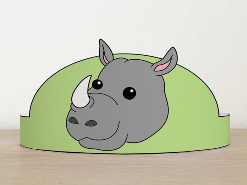 May include: A green and gray paper crown with a cartoon rhinoceros face. The rhinoceros has a large, gray horn and small, black eyes.