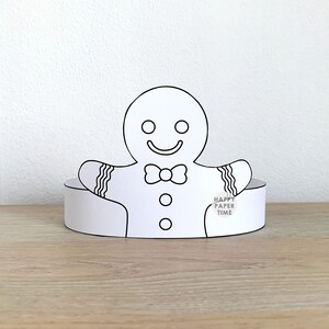 May include: A white paper gingerbread man with a bow tie, buttons, and decorative arm details. The gingerbread man is attached to a white paper base. The text "HAPPY PAPER TIME" is printed on the base. The item is on a wooden surface.