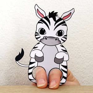 May include: A black and white zebra finger puppet with a grey nose and pink ears. The puppet is made of paper and has a hole for a finger to go through.