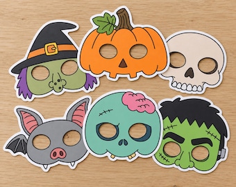 May include: A set of six Halloween-themed paper masks featuring a witch with a black hat, an orange pumpkin, a beige skull, a grey bat, a light blue zombie with a pink brain, and a green monster with black hair and stitches on its face.