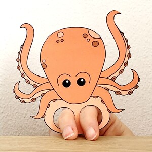 K&ouml;nnte beinhalten: Eine orangefarbene Tintenfisch-Fingerpuppe mit schwarzen Augen und braunen Flecken. Der Tintenfisch hat acht Tentakel mit braunen Ringen.