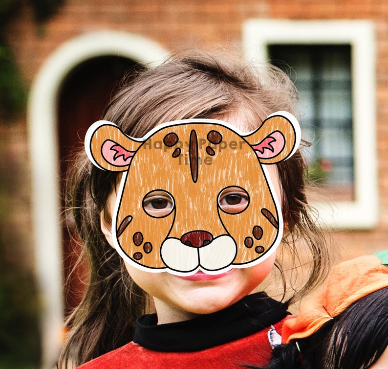 May include: A child wearing a brown and white paper mask of a cheetah. The mask has pink ears and black spots. The child is smiling.