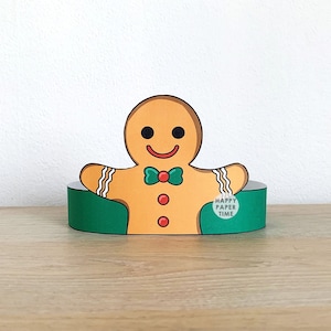 Pode incluir: Um artesanato de papel em forma de homem de gengibre com uma gravata borboleta verde e botões vermelhos. O homem de gengibre está colocado num suporte verde. O texto "HAPPY PAPER TIME" está no lado direito do suporte.