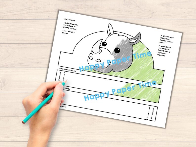 Op de afbeelding: Printbare neushoornkroon knutselmal. De mal bevat een neushoornkop in grijs en wit, een groene achtergrond en instructies voor montage. De tekst "Happy Paper Time" staat op de mal gedrukt.