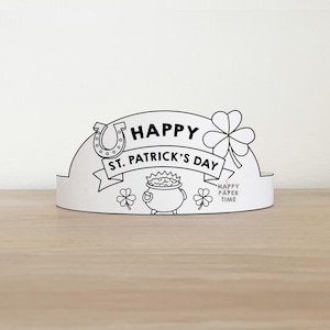 Puede incluir: Una corona de papel blanco con dibujo lineal negro para el Día de San Patricio. La corona presenta una herradura, tréboles, una olla de oro y el texto "HAPPY ST. PATRICK'S DAY". Las palabras "HAPPY PAPER TIME" también están impresas.