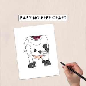 May include: A white paper sheet featuring a black and white cow illustration with black spots, a pink udder, and a dark mouth. The text EASY NO PREP CRAFT is printed at the top. A hand holds a black pen near the paper, which includes a small circular logo.