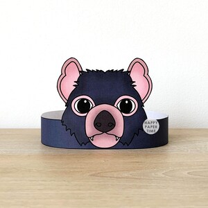May include: A paper craft Tasmanian devil headband. The headband is dark blue with a cartoon illustration of the animal's face in the center. The devil's ears and inner face are pink. The text "HAPPY PAPER TIME" is printed on the side.