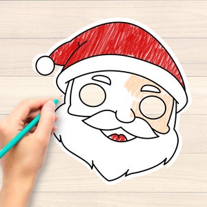 May include: A hand with a teal pencil is colouring a Santa Claus face outline. The Santa face has a red hat, white beard, and a smiling mouth. The background is a light wood grain.