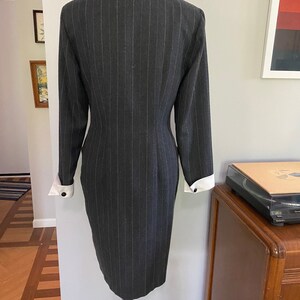 May include: A grey pinstripe dress with white cuffs. The dress has a fitted silhouette and a v-neckline.