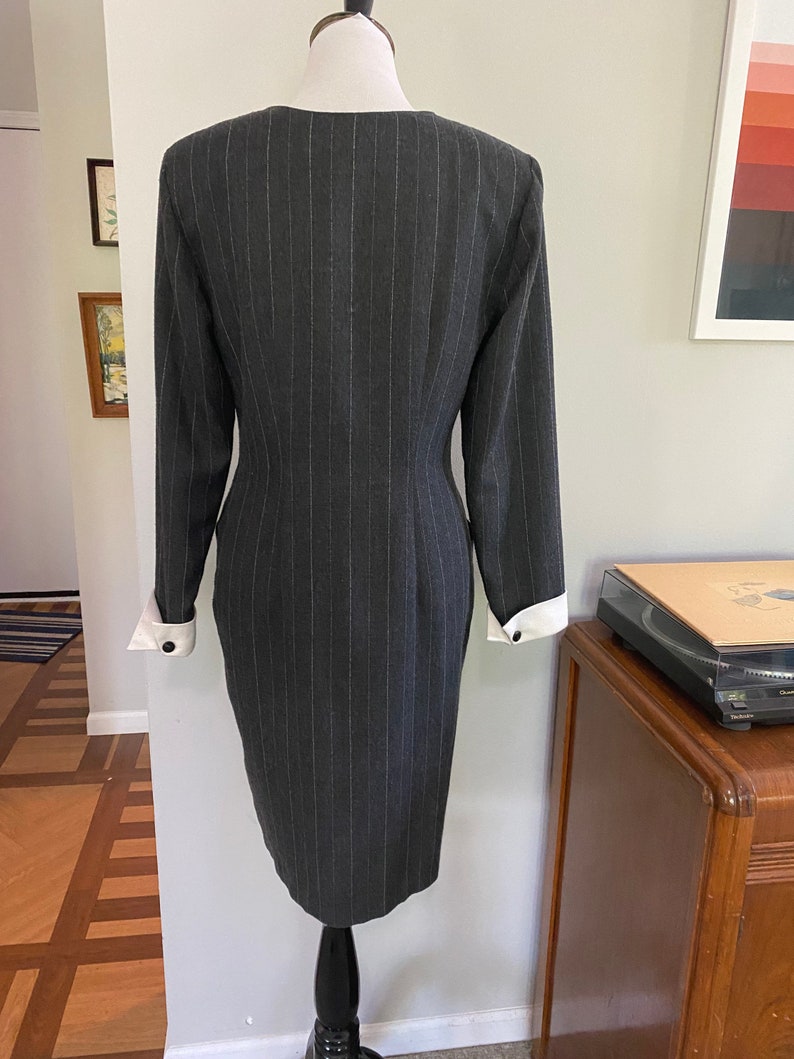 May include: A grey pinstripe dress with white cuffs. The dress has a fitted silhouette and a v-neckline.