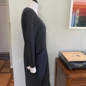 May include: A grey pinstripe dress with a white collar and cuffs. The dress has a button-up front and a pocket on the left side.