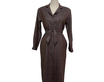 May include: A long-sleeved, button-down dress with a plaid pattern in shades of gray and purple. The dress has a collared neckline, a belt, and a long skirt.